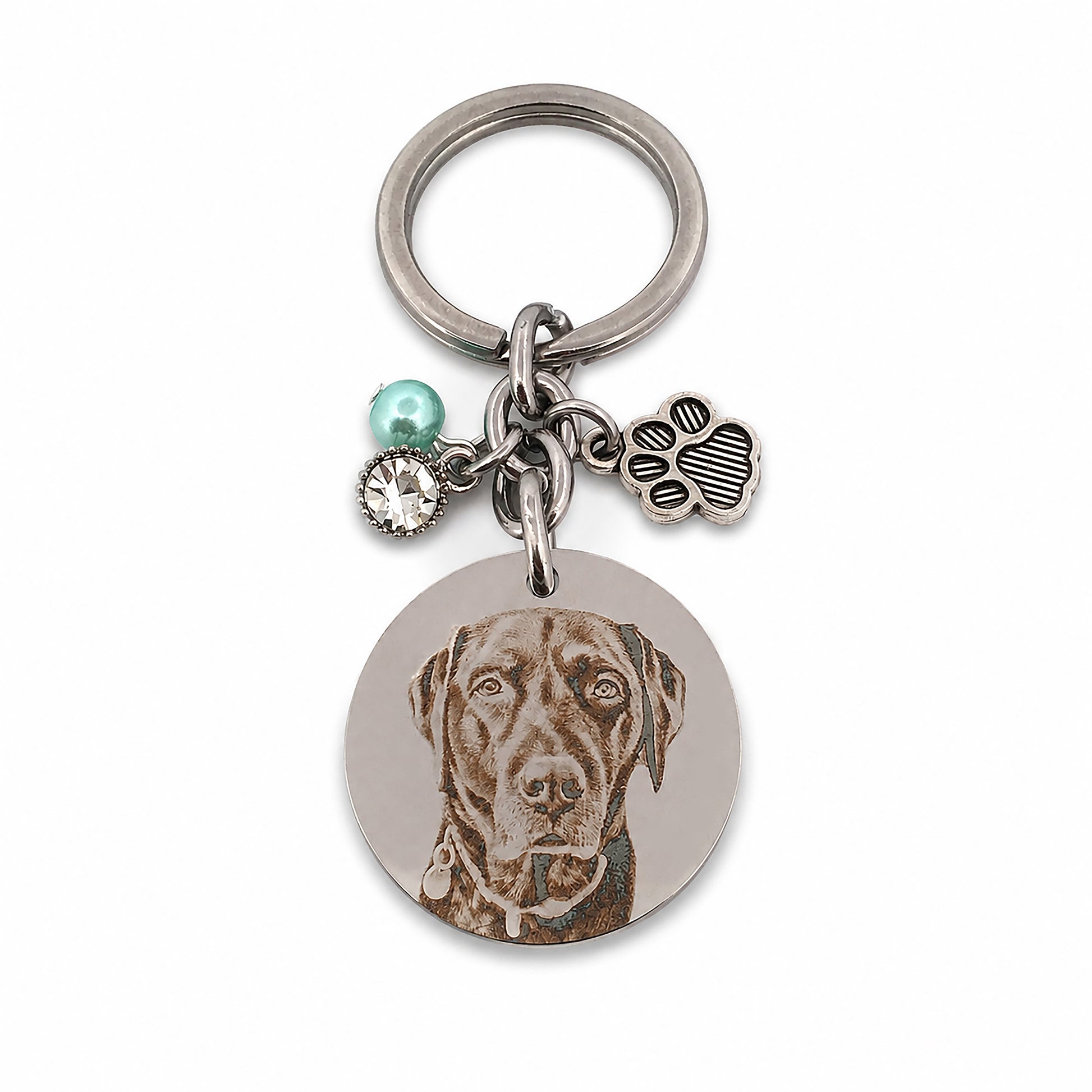 Close-up of a personalised pet memorial keychain featuring a custom engraved dog portrait on polished stainless steel with a paw charm, birthstone bead and crystal accent.