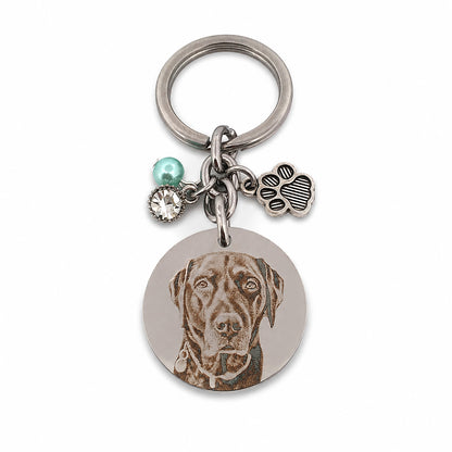Close-up of a personalised pet memorial keychain featuring a custom engraved dog portrait on polished stainless steel with a paw charm, birthstone bead and crystal accent.