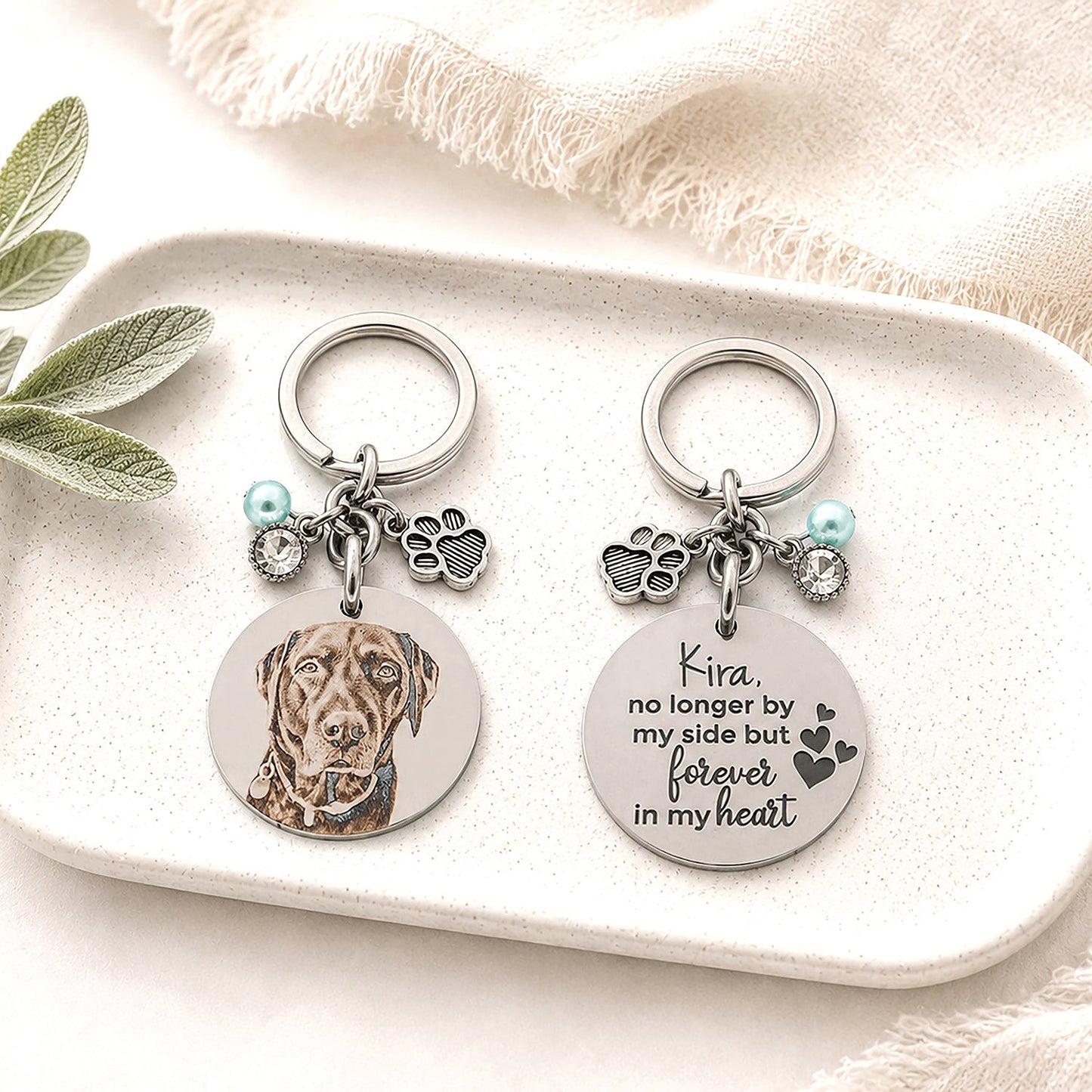 Personalised double-sided pet memorial keychain displayed on a ceramic trinket tray, featuring a custom laser engraved dog portrait on one side and a heartfelt memorial message engraved on the reverse.