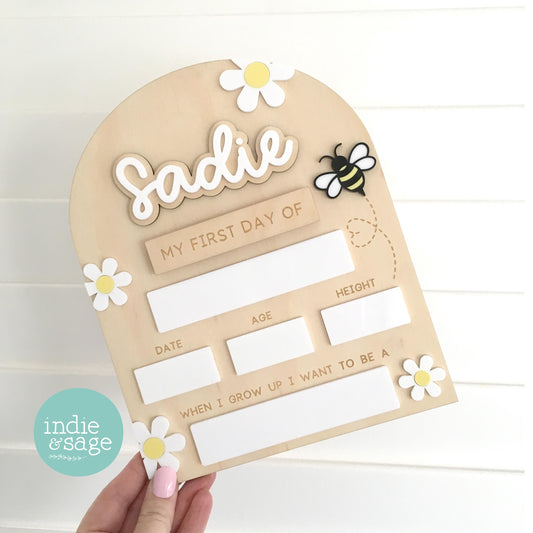 Personalised first day of school board made from natural wood with layered acrylic name detail, featuring milestone sections for age, height and future dreams. Interchangeable back to school board with first and last day plates, with the option to add multiple names, designed as a reusable photo prop for kindergarten and preschool children. Design features stunning white daisys with yellow centres and a little bee. Just so cute and the perfect keepsake piece!